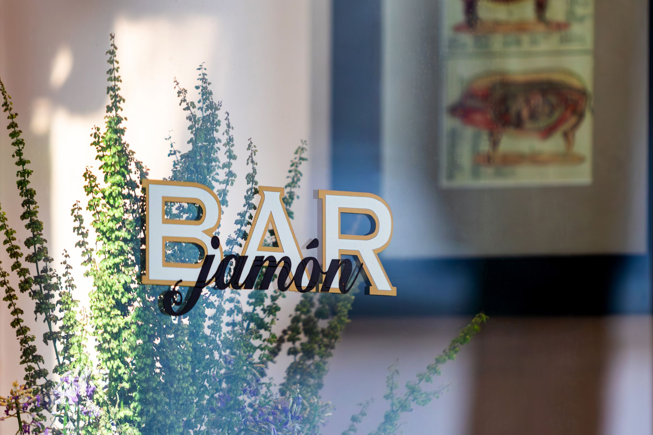 그래머시 뉴욕 시의 윌로우 레지던스 근처에 있는 Bar Jamón 창문 간판에 녹색 식물이 반사되어 있고, 스페인식 타파스를 판매합니다.